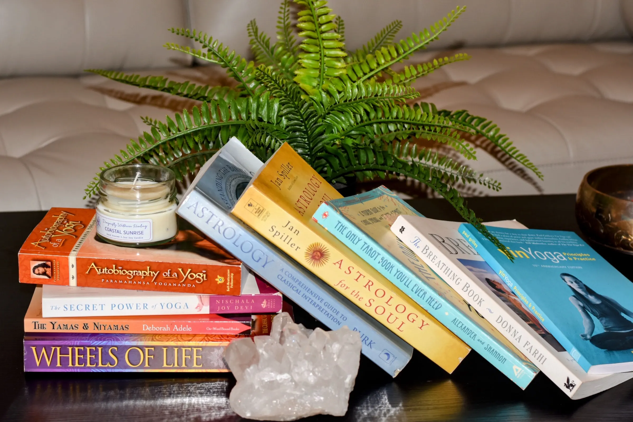A stack of her books on a dark table beside a fern, a quartz crystal and a candle, including Autobiography of a Yogi, Wheels of Life, Astrology for the Soul and The Only Tarot Book You'll Ever Need