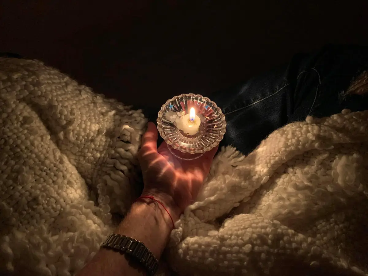 A candle held in cupped hands, resting on a soft blanket in low light