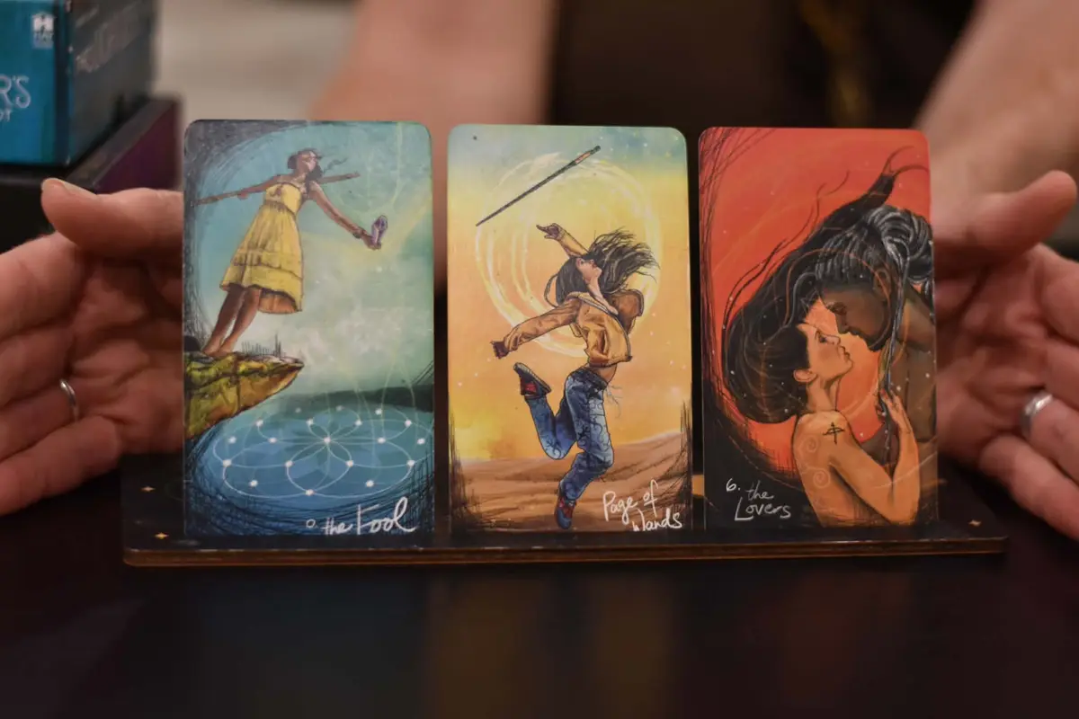 Three tarot cards standing on a wooden holder, held between her hands